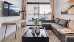 En moderne stue med sofa, sofabord, fjernsyn og et stort vindue.