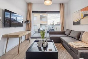 Ein modernes Wohnzimmer mit einer Couch, einem Couchtisch, einem Fernseher und einem großen Fenster.