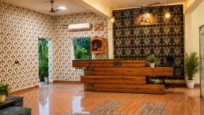 A reception area with a wooden desk, a reception sign, a ceiling fan, and patterned wallpaper. - Wildline Gold Resort (Ramnagar)
