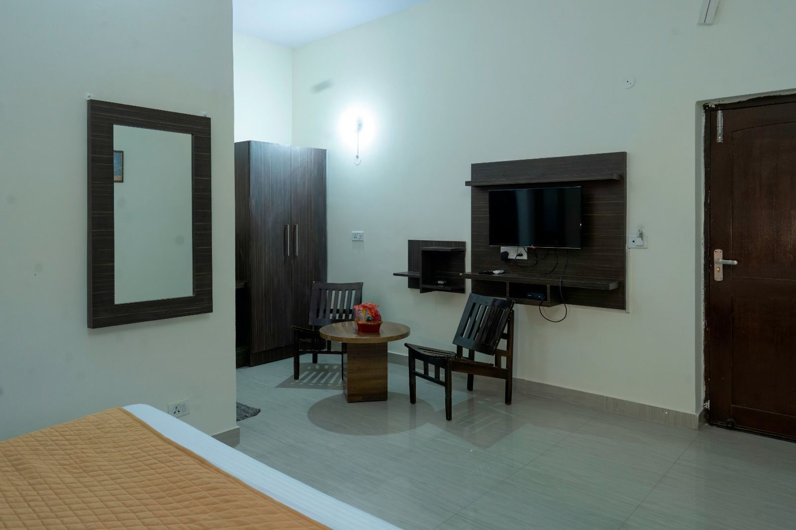 Quarto com cama, televisão na parede, guarda-roupa e uma pequena mesa com cadeiras.