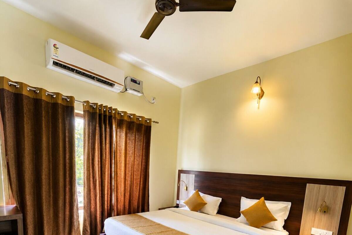 A hotel room with a bed, a ceiling fan, an air conditioning unit, a nightstand, a lamp, and a rug.