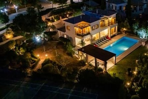 Une maison à deux étages avec une piscine, entourée d’arbres et dotée d’un patio bien éclairé.