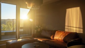 Een woonkamer met een leren bank, een ronde salontafel en uitzicht op een bos door een groot raam.