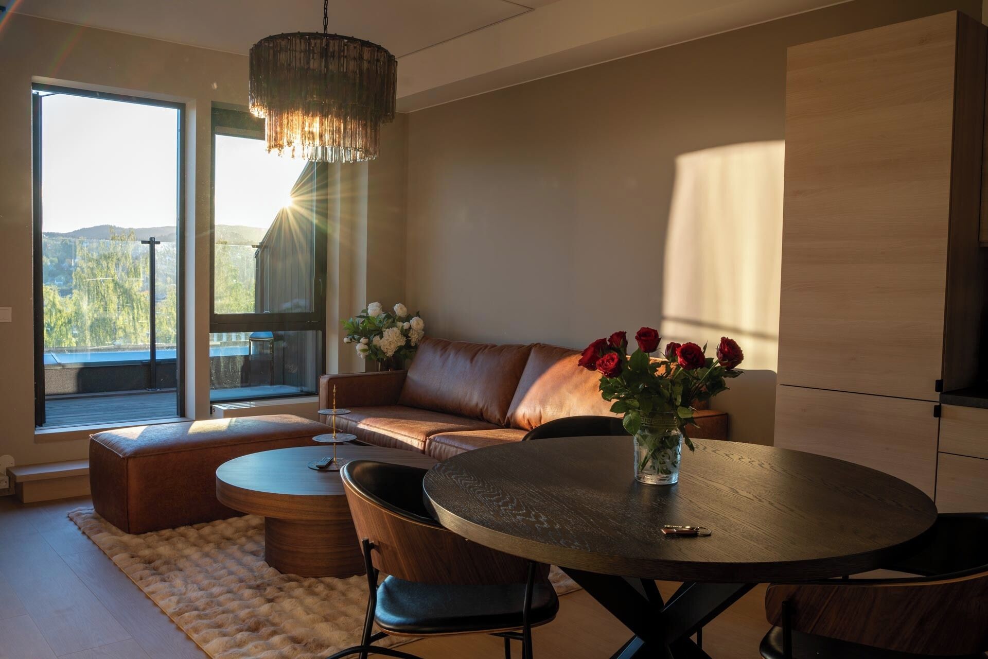 A modern living room with a leather sofa, a round dining table, and a chandelier.