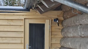 Een houten hutje met een deur, een klein raam en een wandlamp.