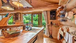 Interior d'una cabana de fusta amb cuina, armaris de fusta, un rentatall i una taula de dinar.