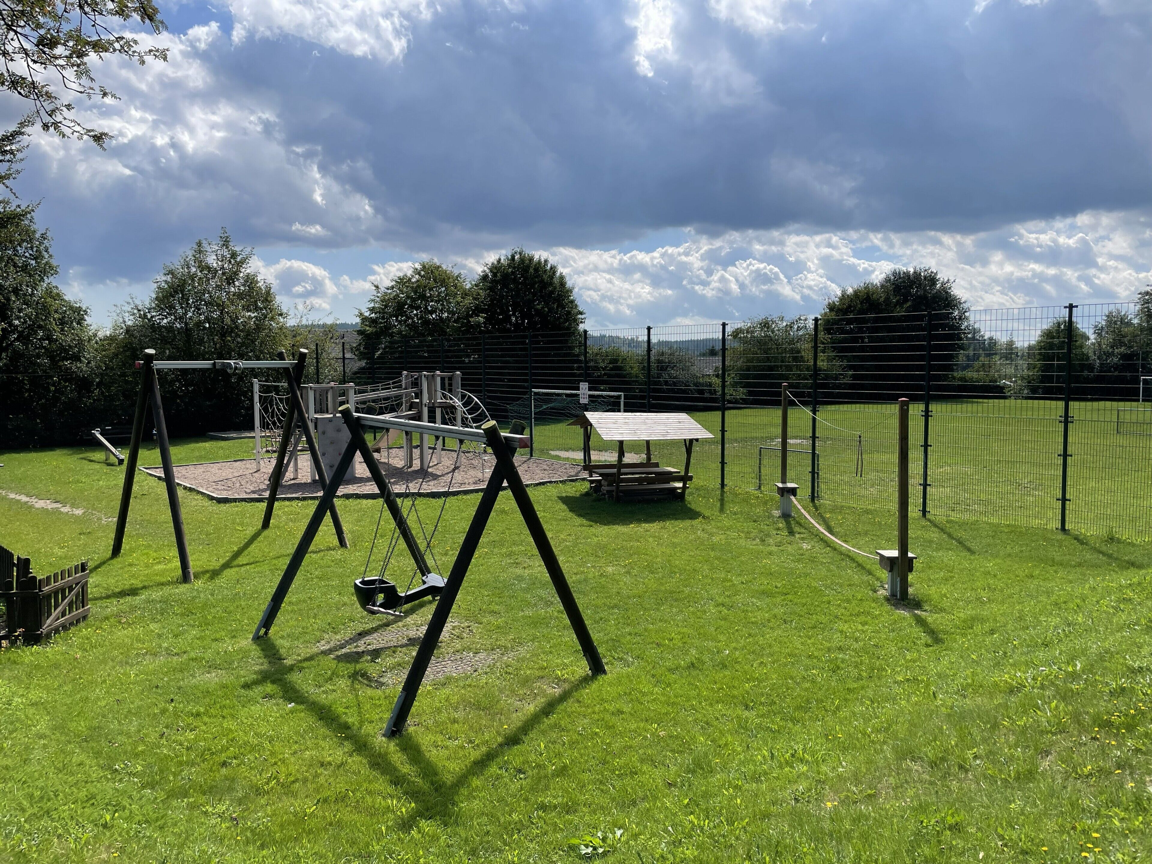 Ein Spielplatz mit Schaukeln, einer Kletterkonstruktion und einem Picknicktisch.