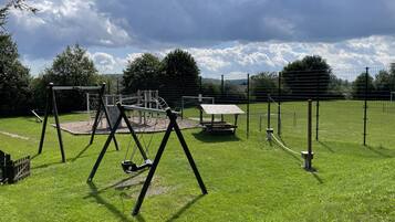 Ein Spielplatz mit Schaukeln, einer Kletterkonstruktion und einem Picknicktisch.