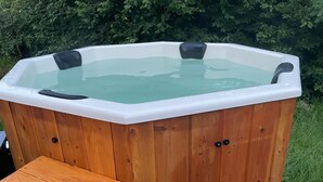 A wooden hot tub with a bench, surrounded by greenery.