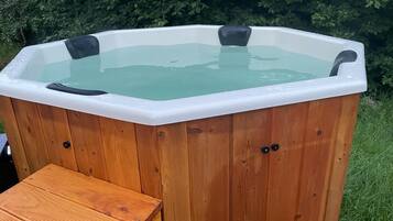 Ein hölzernes Whirlpool mit Sitzbank, umgeben von viel Grün.