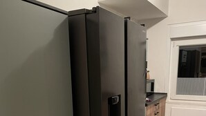 A kitchen with two black refrigerators, a wooden cabinet, and a window.