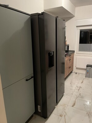 A kitchen with two black refrigerators, a wooden cabinet, and a window. - Attractive detached house with hot tub (Winterberg)