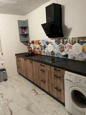 Cocina con armarios de madera, campana extractora negra, lavadora y salpicadero de azulejos con motivos de estaciones.