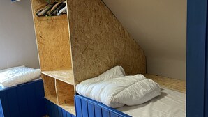 A room with a bunk bed, wooden shelves, and a sloped ceiling.