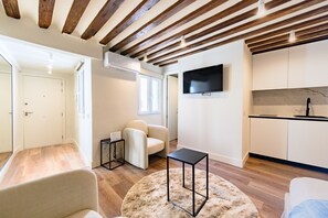 A modern living room with a sofa, a round rug, a TV, and a kitchen area with cabinets and a countertop. - (ESC2225) Study in the Center of Madrid (Madrid)