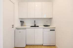 Eine kleine Küche mit weißen Schränken, einem Spülbecken, einem Geschirrspüler und einem kompakten Kühlschrank.