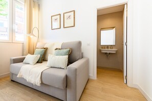 Ein neutral eingerichtetes Wohnzimmer mit Sofa, Kissen, einer Lampe und einem gerahmten Bild an der Wand.