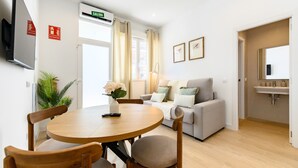 A living room with a round wooden table, two chairs, a sofa, a TV, and a window with curtains. - (SDB1L2) 1 bedroom apartment in Tetuán, Madrid (Madrid)
