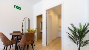 Un coin repas comprenant une table et des chaises, un miroir, une plante en pot et une porte-fenêtre donnant sur une cuisine.