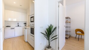 Une cuisine moderne avec des meubles blancs, un lave-vaisselle et un four. On y trouve également une plante en pot et une chaise.