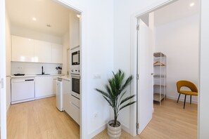 Eine moderne Küche mit weißen Schränken, einem Geschirrspüler und einem Backofen. Eine Topfpflanze und ein Stuhl stehen im Raum.