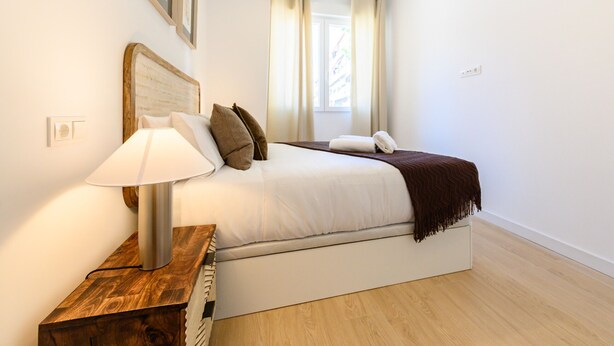 Une chambre à coucher avec un lit, une lampe de chevet et une fenêtre avec des rideaux.