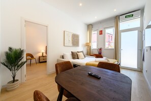 Ein Hotelzimmer mit Bett, Esstisch, Stuhl, Lampe und einem Blumentopf.