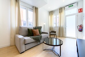 A modern living room with a sofa, a glass coffee table, a chair, and a door with an 'EXIT' sign. - (SDB1L4) 1 bedroom apartment in Tetuán, Madrid (Madrid)