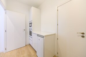 A narrow hallway with white doors, a small kitchen area with a refrigerator and oven, and a wooden floor. - (SDB1L4) 1 bedroom apartment in Tetuán, Madrid (Madrid)