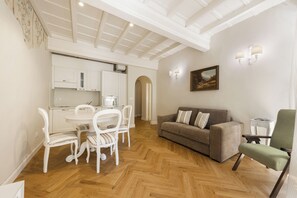 A dining area with white chairs and a table, a sofa, and a painting on the wall. - Emma by MMega (Firenze)