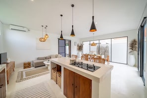 Una cocina moderna con una isla central, iluminación colgante y un comedor con vistas.