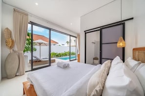 Un dormitorio con una cama grande, una puerta corrediza a una piscina y vistas a un edificio con tejado rojo.
