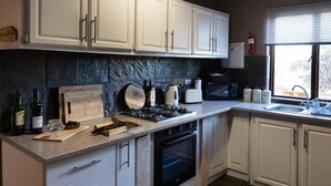 A kitchen with white cabinets, a stone backsplash, a gas stove, a microwave, and a window with blinds.