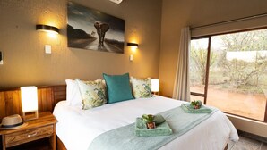 A hotel room with a large bed, two bedside tables, a nightstand, a window with a view, and wall-mounted lighting.