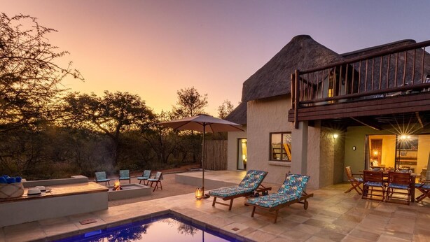 A pool area with lounge chairs, a fire pit, and a thatched-roof structure.