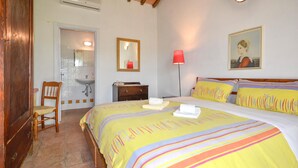 Ein Schlafzimmer mit einem Bett, einem Sessel, einer Kommode, einem Nachttisch, einer Lampe, einem Spiegel und einem Bild an der Wand.