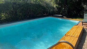 Ein rechteckiger Swimmingpool mit klarem, blauem Wasser, umgeben von einer Holzterrasse und üppiger Vegetation.