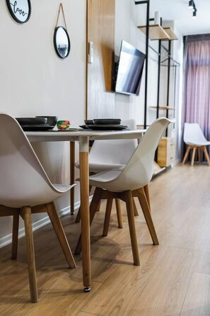Un comedor moderno con una mesa blanca, cuatro sillas y un televisor de pantalla plana montado en la pared.