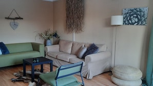 A living room with two sofas, a small table, a chair, a decorative plant, a wall hanging, and a lamp. - Going North (Molkom)