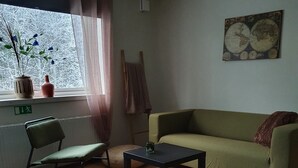 A room with a green sofa, a black table, a striped bed, a chair, a window with curtains, a radiator, and a wall-mounted globe. - Going North (Molkom)