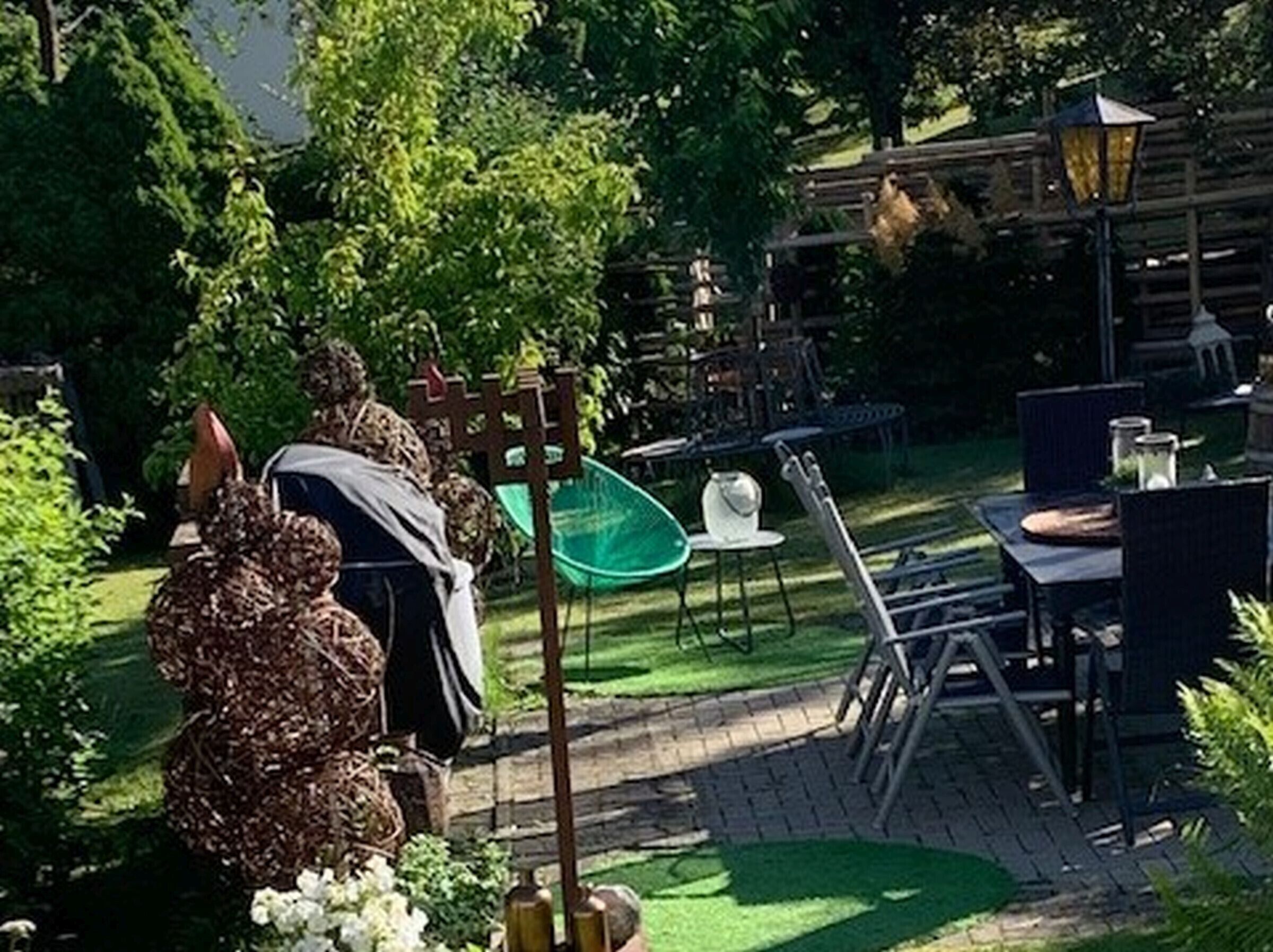 Ein Garten-Sitzbereich mit Gartenmöbeln, einem Zierzaun und einem kleinen Tisch mit Stuhl.