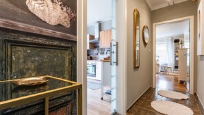 Un couloir avec une porte en bois, un coin cuisine et un espace de vie agrémenté d’un tapis blanc et d’un miroir.