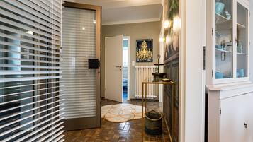 A hallway with a door, a radiator, a patterned rug, a small table with a candle, and a cabinet with glass doors.