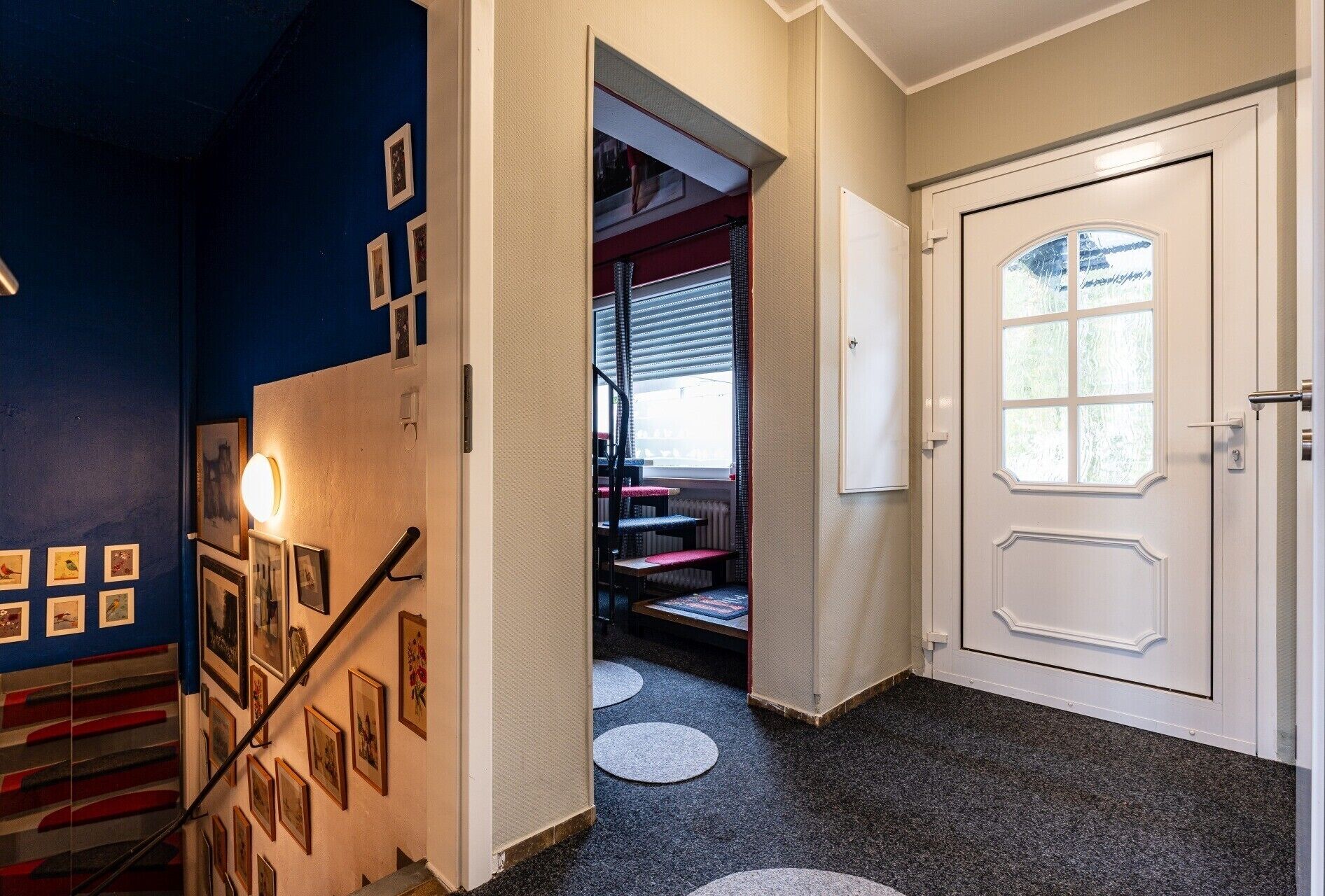 Een gang met een trap, een deur met een raam en een muur met ingelijste foto's.