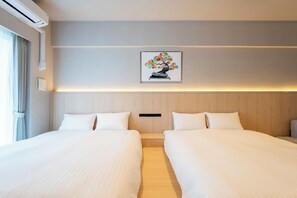 Una habitación de hotel con dos camas, aire acondicionado de pared, una mesita de noche, una lámpara de noche, una obra de arte enmarcada y una ventana con cortinas.