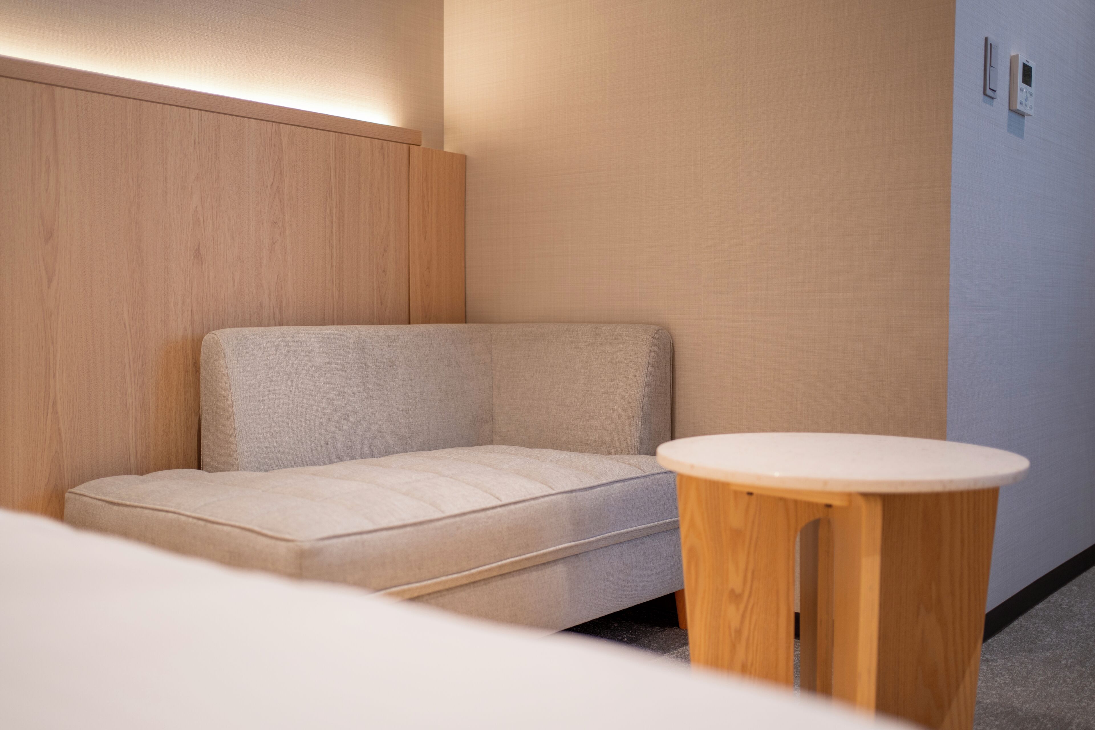 A modern room with a sofa, a round wooden table, and a wall-mounted light fixture.