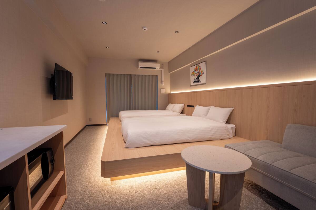 Una habitación de hotel moderna con una cama grande, un sofá, una pequeña mesa redonda, un televisor de pantalla plana y un equipo de aire acondicionado.