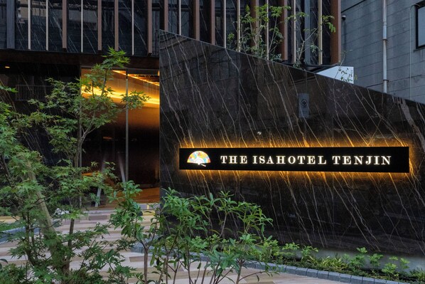 L’entrée d’un hôtel, avec une enseigne indiquant « The Isahotel Tenjin », et la façade moderne du bâtiment.