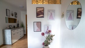 Un interior modern amb un terra de fusta, una paret blanca amb obra emmarcada, un mirall rodó i un vas amb flors.