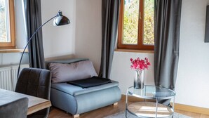 Un saló modern amb un sofà, una taula de centre de vidre, una làmpada i vista a vegetació a l'exterior.